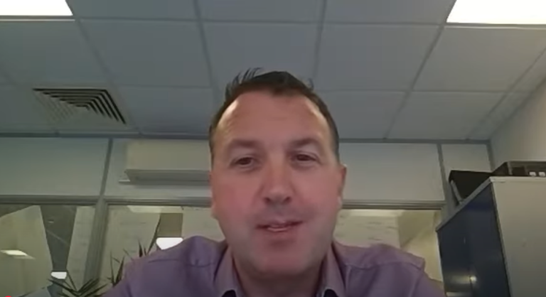 Professional on a video call in an office setting, speaking to camera during an online meeting or virtual presentation.