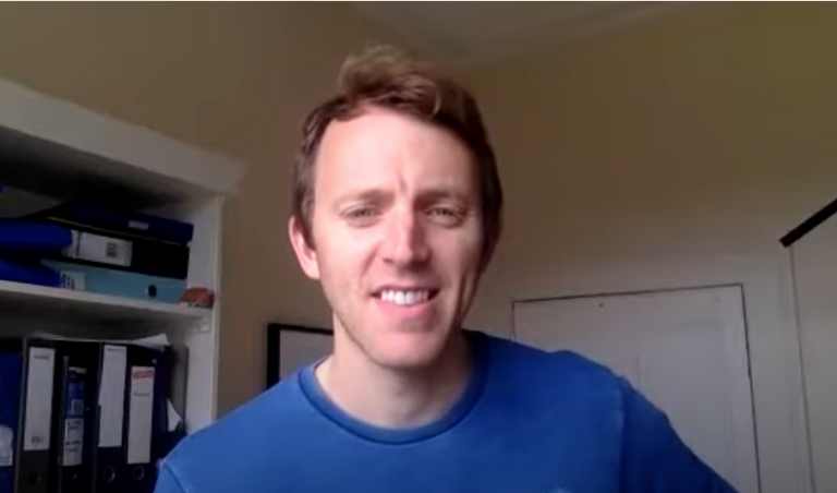 Professional smiling during a video call from a home office setting, speaking to camera during an online meeting or virtual discussion.