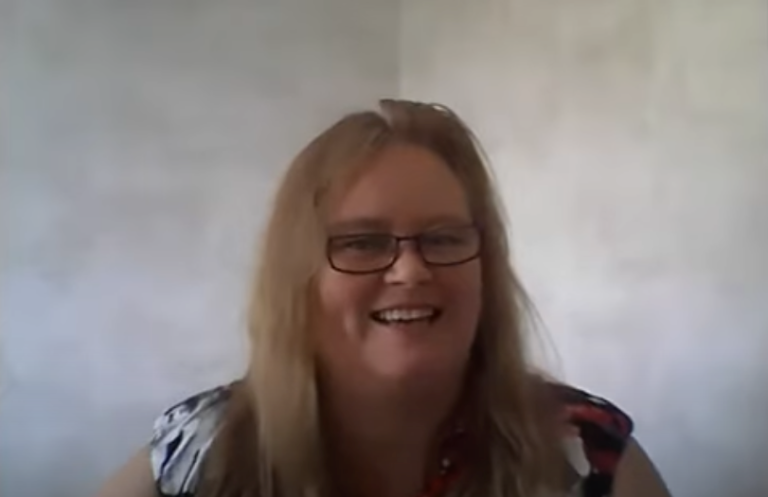 Professional smiling during a video call, speaking from a home or remote office setting.