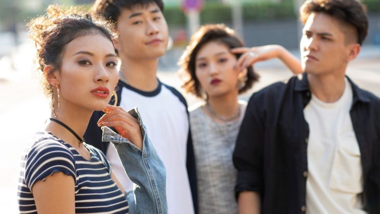 Group of four young adults standing outdoors together, posing casually in an urban setting.